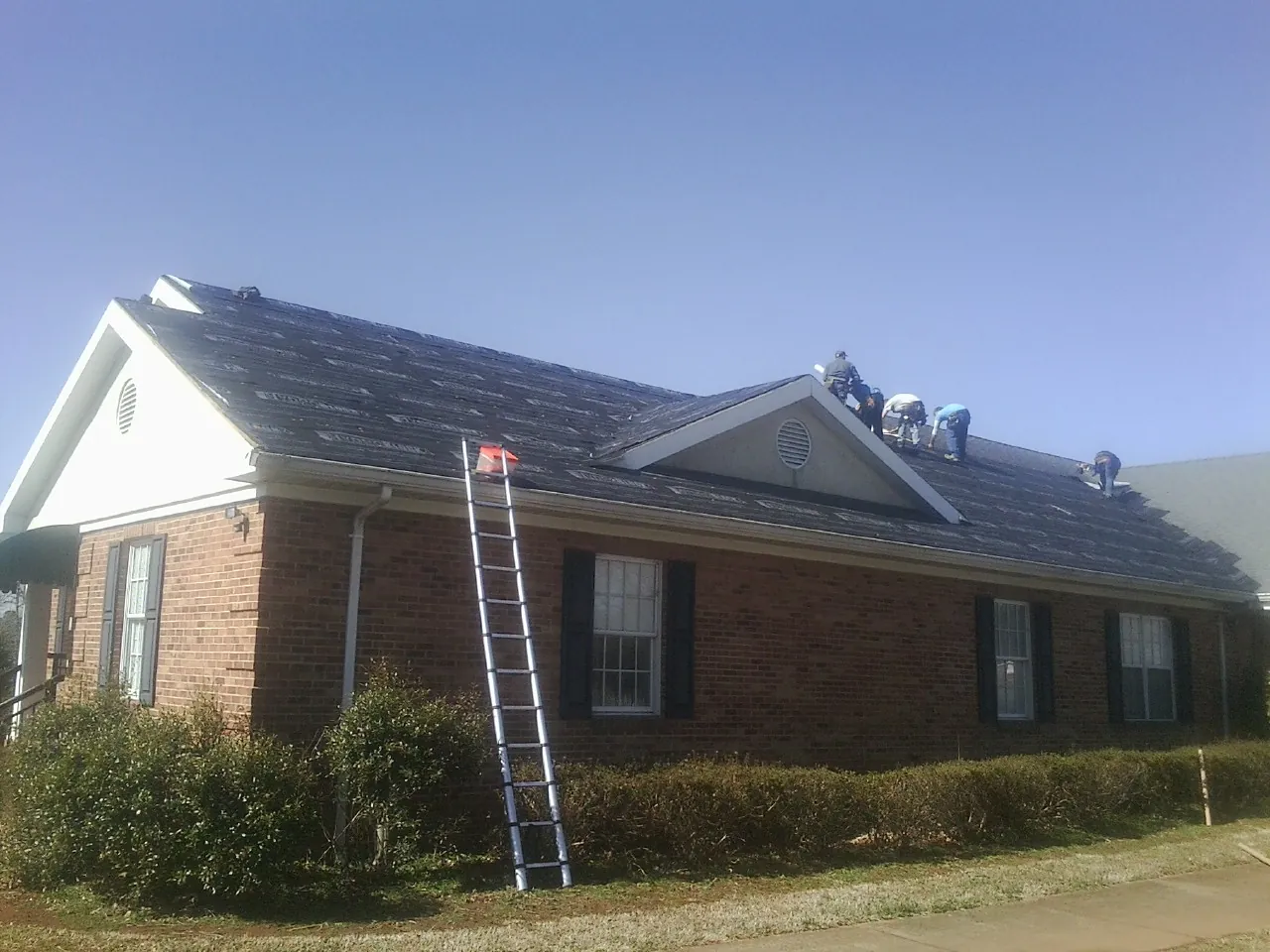 Crew tearing shingles off a brick ranch roof with a ladder set — Emergency Roof Repair work by our crew in Mize