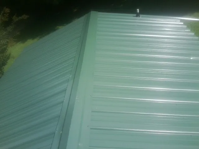 New green metal panels meeting at the ridge of a roof — Flat Roof Repair work by our crew in Mize