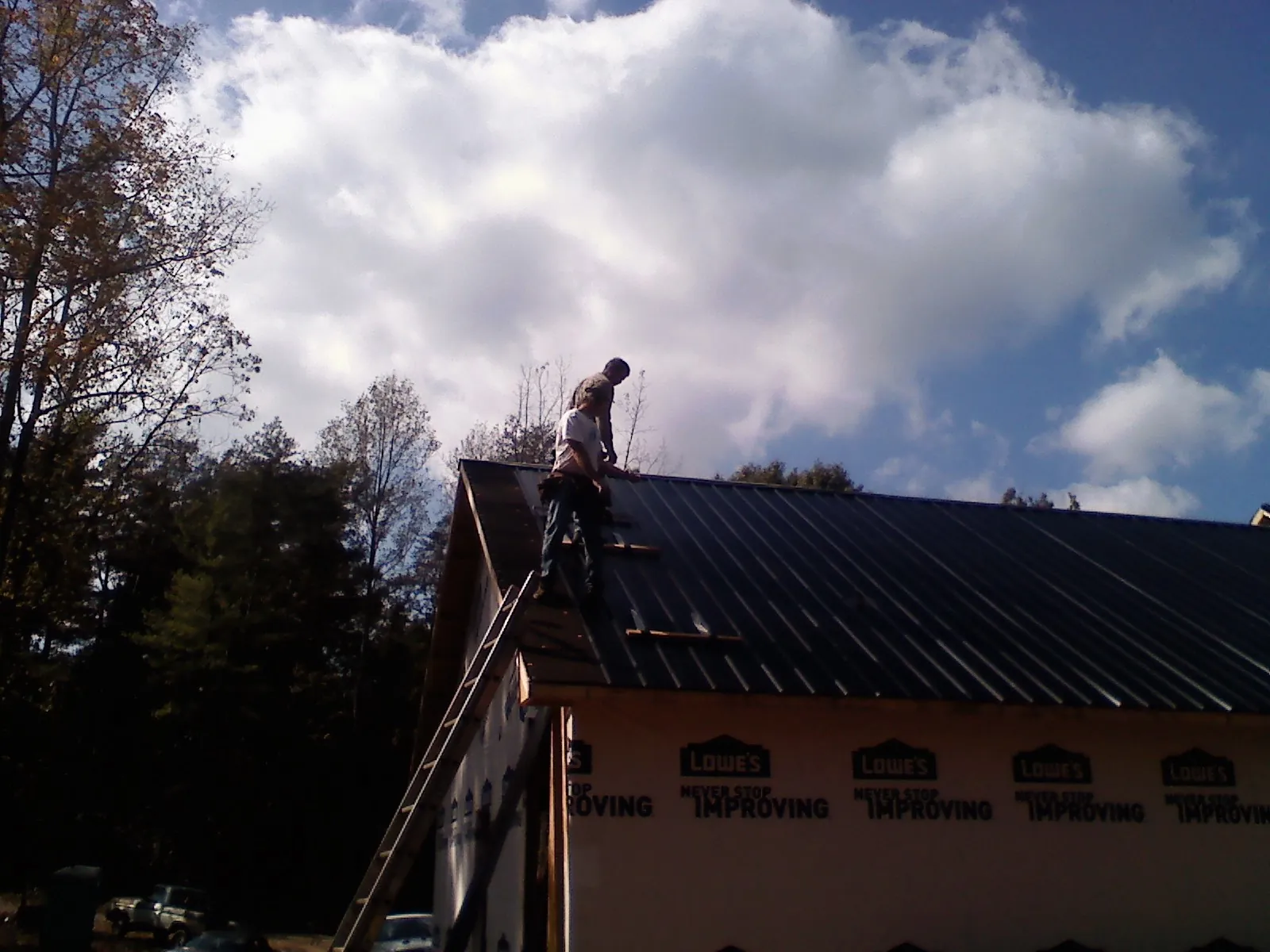 Roofer fastening dark metal panels high against a cloudy sky, from a Roof Inspection job in Mize